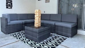 Un canapé modulable, une tour de blocs en bois et un tapis à motifs dans un espace de détente extérieur au design moderne.