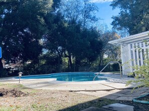 Un giardino con piscina, un pergolato e un'area recintata.