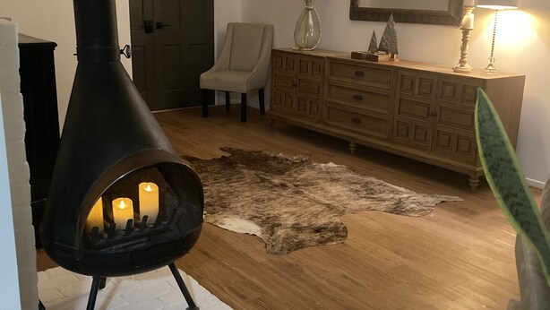 Un salon avec un poêle à bois noir, un meuble en bois, une chaise, un tapis et un miroir accroché au mur.