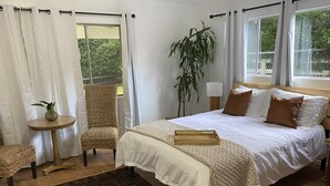 Une chambre avec un grand lit, une petite table, une chaise et une plante en pot.