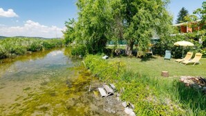 A riverside property with a clear water body, lush greenery, and outdoor seating.