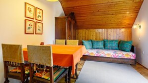 A cozy room with a wooden ceiling, a bed with colorful pillows, a dining table with chairs, and framed pictures on the wall.