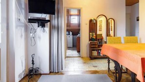A room with a wooden ceiling, a flat-screen TV mounted on the wall, a dining table with yellow chairs, and a mirror with three panels.