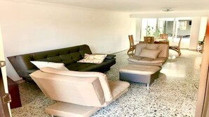Een woonkamer met een zwarte bank, beige fauteuils en een klein voetenbankje.