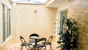 Een klein, afgesloten terras met een ronde tafel en vier stoelen, een plant in pot en een dakraam.