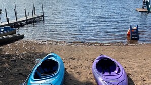 Zwei Kajaks am sandigen Strand eines ruhigen Sees, im Hintergrund ein Steg.