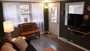 Ein Wohnzimmer mit einer Couch, einer Holzbank, einem Couchtisch, einem Fernseher auf einem Schrank und einer Lampe.