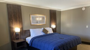 A hotel room with a large bed, two bedside tables with lamps, a framed picture on the wall, and a carpeted floor.