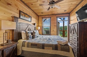 A wooden cabin bedroom with a bed, dresser, ceiling fan, and large windows. - Best Location w/ Views, KING Beds, 3 TV Gaming Wall, and Giant Scrabble Board (Sevierville)