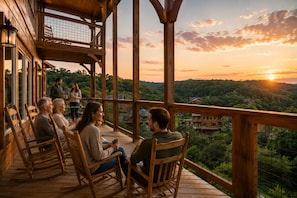 A wooden deck with rocking chairs, a covered area with a railing, and a scenic view of a forested landscape.