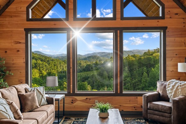 A cozy room with a large window offering a view of a forested mountain range.