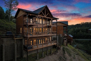A multi-story wooden cabin with balconies, a car parked outside, and a scenic view of the surrounding forest.