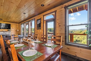 Une salle à manger en bois avec une table dressée pour quatre personnes, de grandes fenêtres et une vue sur l’extérieur.