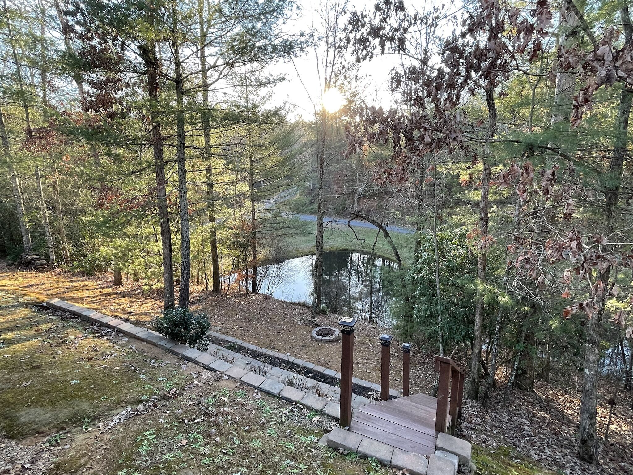 Une terrasse en bois qui mène à un étang entouré d’arbres.