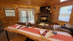 A cozy cabin interior with a wooden interior, a fireplace, a television, and a dining area with a table set for two.