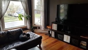 Relax in this inviting living room with a sofa by the window, a TV, bookshelf, and a potted plant.