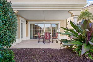 Relax in a serene garden setting with a patio featuring a seating area and large window.
