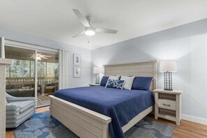 Un dormitorio con cama, dos mesitas de noche, ventilador de techo y vistas a través de un ventanal corredero.