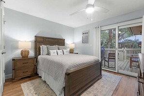 Un dormitorio con una cama de madera, dos mesitas de noche, un ventilador de techo y vistas a una terraza a través de una puerta corrediza de vidrio.