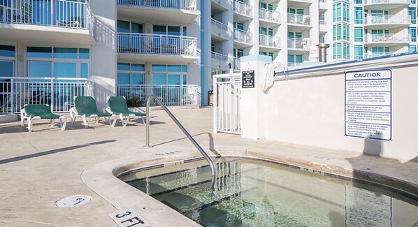 A swimming pool area with a caution sign, a pool ladder, and green lounge chairs.