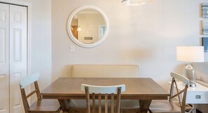 Un comedor con una mesa de madera y dos sillas, un espejo redondo en la pared y una lámpara sobre una mesita auxiliar.
