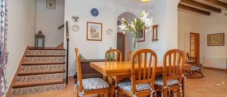 Un coin repas avec une table et des chaises en bois, un escalier orné de carreaux décoratifs et un plafond avec des poutres apparentes.