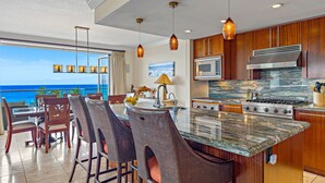 A kitchen with a large island, bar stools, a stove, and a view of the ocean.