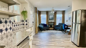 A modern kitchen with a granite countertop, a stainless steel refrigerator, and a dining area with two sofas and a coffee table. - Games Galore & Rooftop Deck by St. Mary's, BMT (San Antonio)