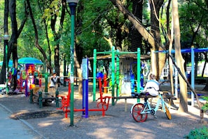 Explore the playground area surrounded by trees, featuring swings, slides, and climbing frames.