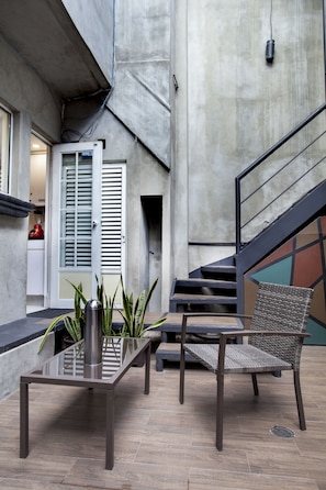 Relax in this inviting outdoor seating area with a metal table and wicker chair, surrounded by a concrete wall and a staircase.