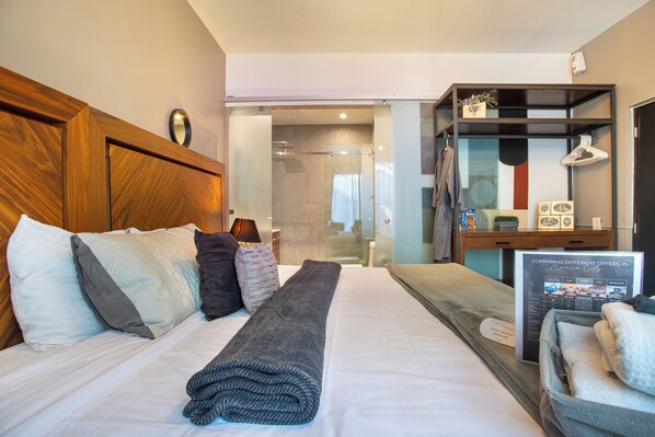 Ein Hotelzimmer mit einem großen Bett, einem Holzkopfstück, einem Nachttisch mit Lampe, einem Spiegel und Blick ins Bad.