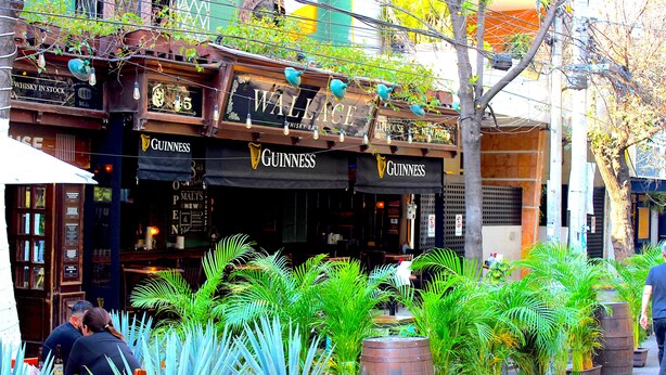 A bar with Guinness signage, outdoor seating, and potted plants. - Deluxe Room in Condesa + Rooftop & Coworking - Beta by Nomadier (Ciudad de México)