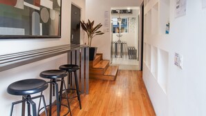 A hallway with wooden flooring, a bar area with stools, a hanging light fixture, and a large abstract painting on the wall. - Deluxe Room in Condesa + Rooftop & Coworking - Beta by Nomadier (Ciudad de México)