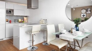 Una cocina moderna con armarios blancos, una isla central con taburetes y un comedor con mesa y sillas de vidrio.