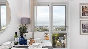 Un comedor con una mesa dispuesta para dos personas, vistas a la ciudad a través de amplios ventanales y cuadros en la pared.