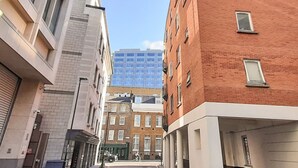Una stretta via fiancheggiata da edifici moderni e tradizionali, tra cui un palazzo in mattoni rossi e un grattacielo in vetro sullo sfondo.
