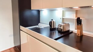 Una cucina moderna con mobili bianchi, un piano di lavoro nero, un bollitore, un tostapane e un portacoltelli.