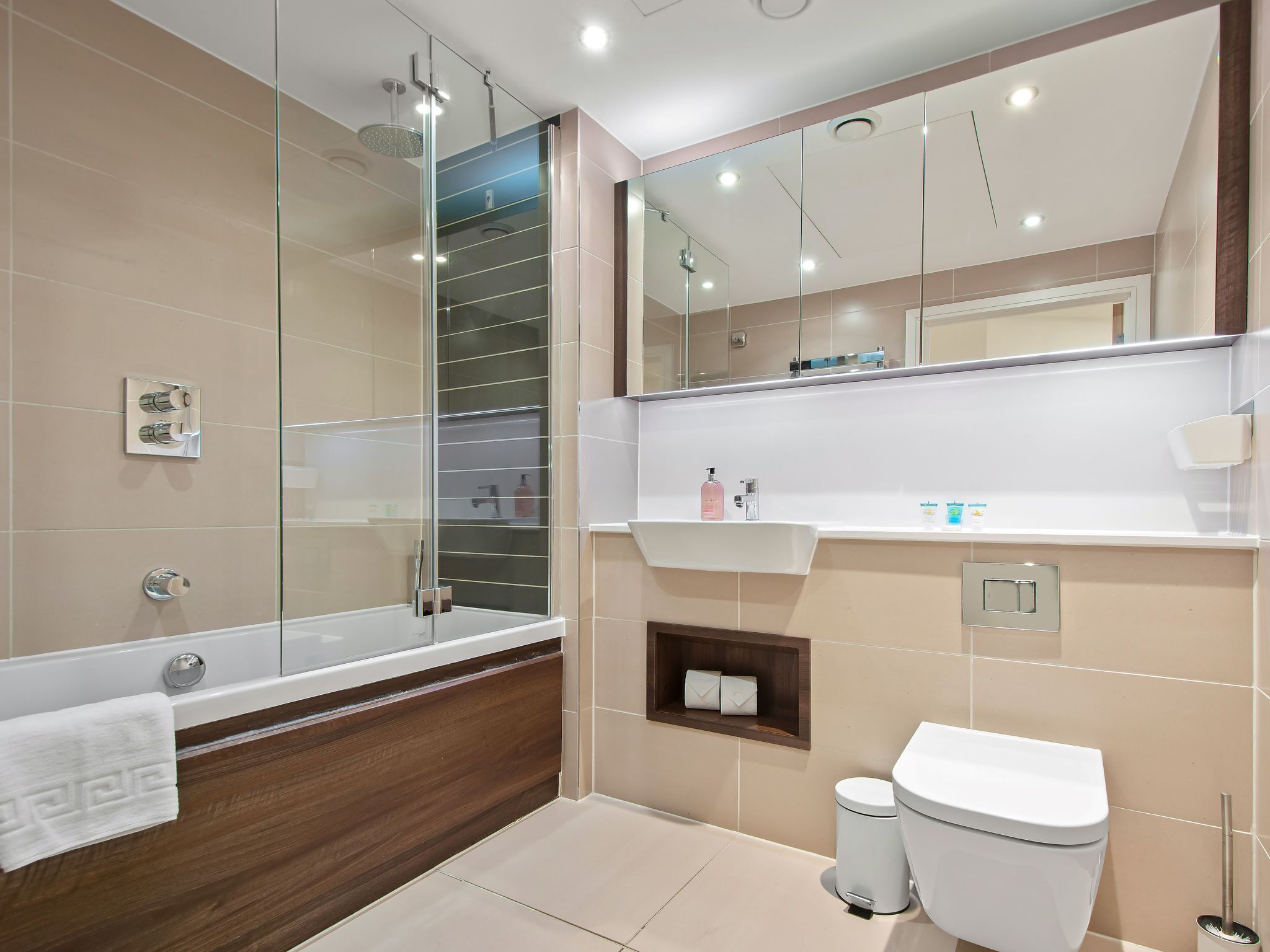 A modern bathroom with a glass shower enclosure, a wooden vanity, a white toilet, and a mirror above the sink.