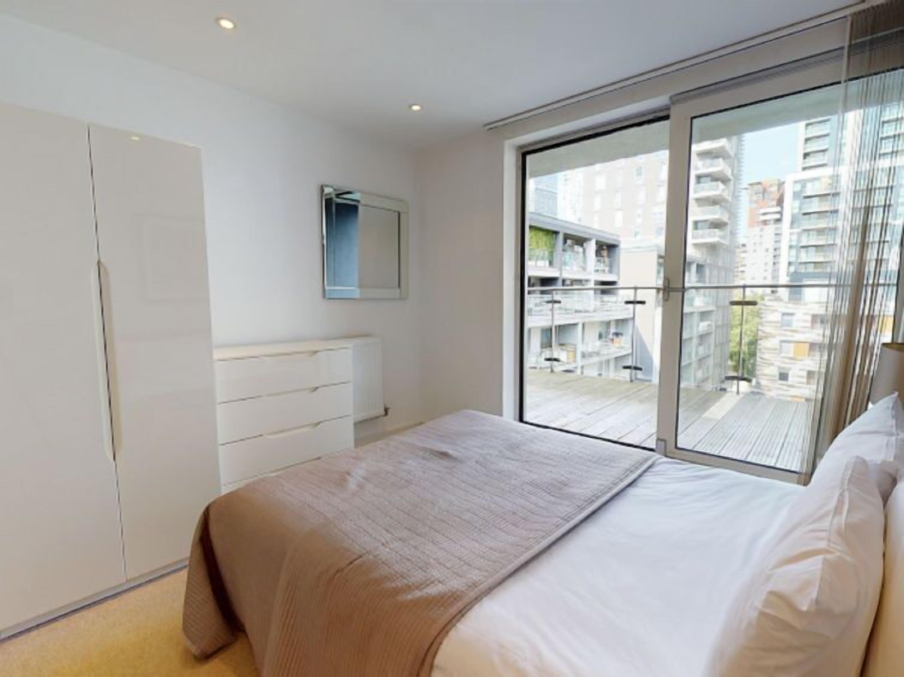 A modern bedroom with a large bed, a wardrobe, and a sliding glass door leading to a balcony.