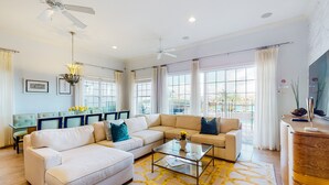 Un salon spacieux avec un canapé beige, une table basse en verre et un ventilateur de plafond.