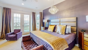Une chambre avec un grand lit, un ventilateur de plafond, un lustre et une vue par la fenêtre.