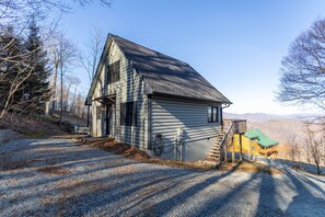 A log cabin with a steep roof, a front porch, and a staircase leading to a second-story deck.