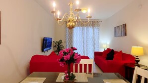 Un comedor con una mesa, sillas, una lámpara de araña, un sofá rojo, un televisor y una planta.