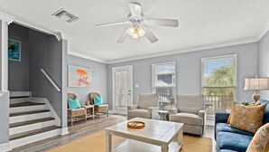 A spacious living room with a staircase, a ceiling fan, and a large window with blinds.