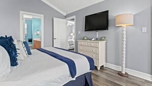 A bedroom with a bed, dresser, TV, and floor lamp.