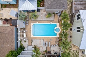 Una piscina rectangular con un pequeño jacuzzi circular, rodeada de palmeras y una terraza con sillones de descanso.