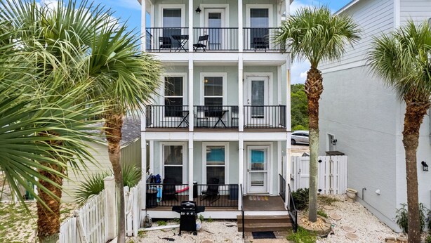 A two-story building with balconies, a white picket fence, and palm trees.