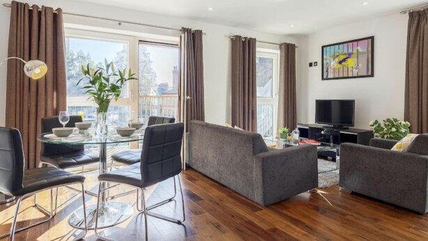 Una sala moderna con una mesa de comedor de cristal, sofás grises y un televisor de pantalla plana.