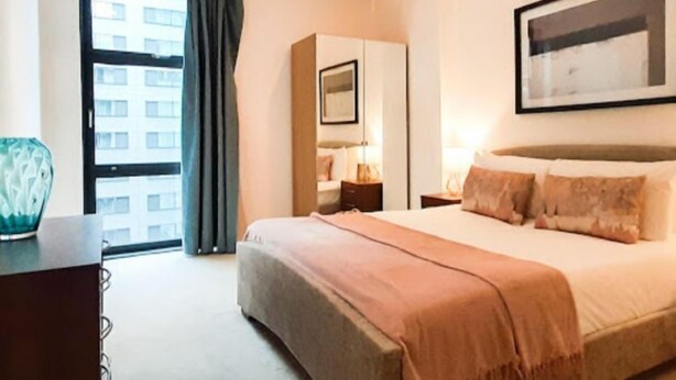 Una habitación de hotel con una cama grande, un escritorio, una silla, una ventana con cortinas y un cuadro en la pared.