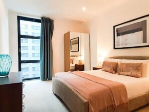 A hotel room with a large bed, a desk, a chair, a window with curtains, and a framed picture on the wall. - Discovery Dock by Interhome (Canary Wharf)